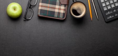 Office desk table with notepad, supplies and coffee. Dark workspace tabletop with copy space. Top...