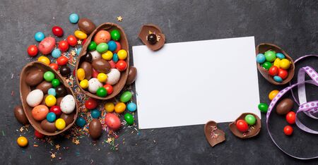 Chocolate easter eggs and colorful sweets on stone background greeting card. Top view with copy...