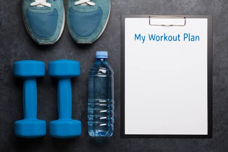 Fitness equipment and blank sheet for workout plan on a stone background. Top view flat lay with...