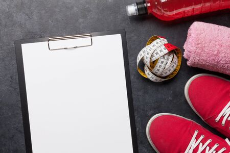 Fitness equipment and blank sheet for workout plan on a wooden background. Top view flat lay with...