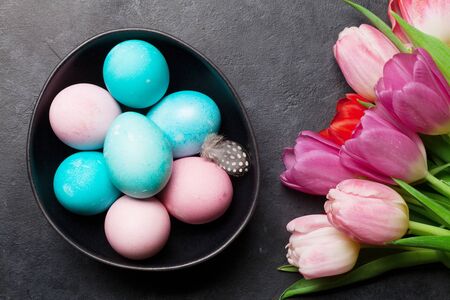 Easter greeting card with easter eggs and tulip flowers over stone background. Top view flat lay