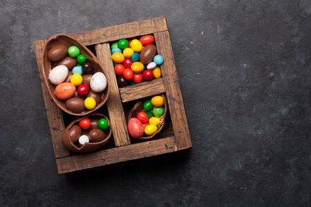 Chocolate easter eggs and colorful sweets on stone background greeting card. Top view. Flat lay with...