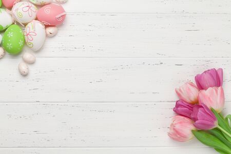 Easter greeting card with easter eggs and tulip flowers over wooden background. Top view flat lay...
