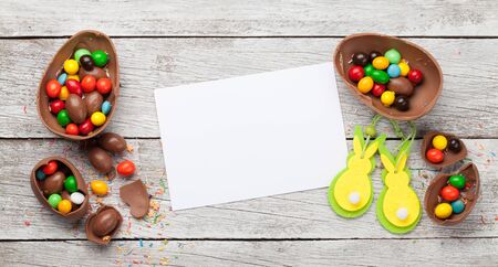 Chocolate easter eggs and colorful sweets on wooden background greeting card. Top view. Flat lay...