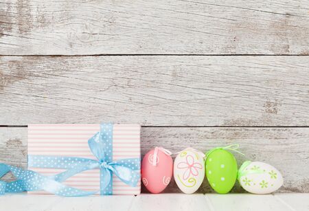 Easter greeting card with colorful easter eggs and gift box in front of wooden wall. With space for...