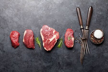 Variety of fresh raw beef steaks with spices on stone background. Top view flat lay with copy spaceの写真素材