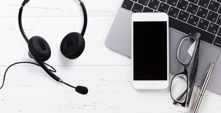 Office workplace table with supplies, smartphone, headset and laptop.