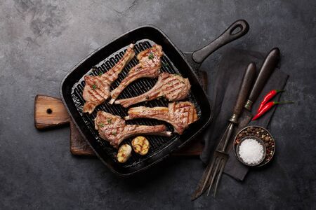 Grilled lamb ribs in frying pan. Hot rack of lamb with spices and condiments. Top view on stone...