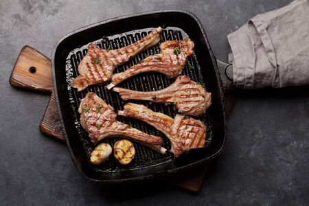 Grilled lamb ribs in frying pan. Hot rack of lamb with spices and condiments. Top view on stone tableの写真素材