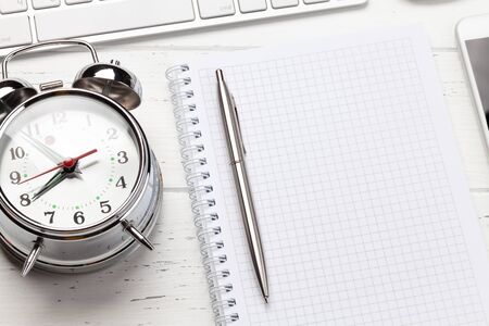 Workplace desk table with computer, supplies and alarm clock.