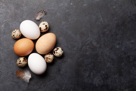 White, brown and quail eggs on stone table.