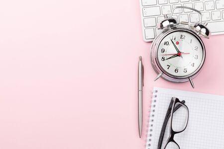 Pink workplace desk table with computer, supplies and alarm clock.の写真素材