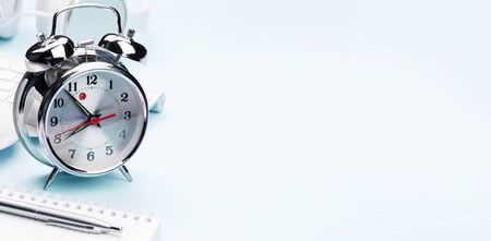 Blue workplace desk table with computer, supplies and alarm clock. Morning or deadline concept. With...