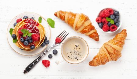 Delicious homemade pancakes with summer berries and jam, croissants and coffee for breakfast. Top viewの写真素材