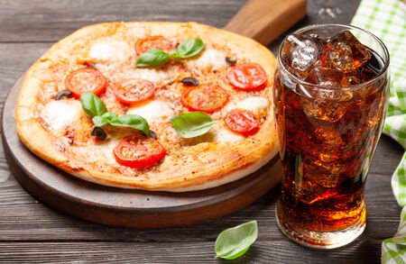 Glass of cola with ice and tasty homemade pizza with garden tomatoes, cheese and basilの写真素材