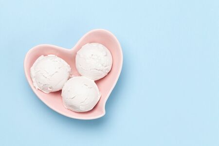 Vanilla ice cream scoops in heart shaped bowl on blue background. Top view with copy spaceの写真素材