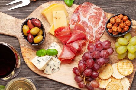 Cheese, meat, grapes and olives antipasto. Appetizer selection on wooden board and glasses with red...