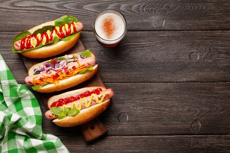Various hot dog with vegetables, lettuce and condiments and beer glass on wooden background. Top view with copy space. Flat layの写真素材