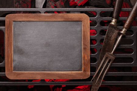Metal barbecue grill over hot coal, knife and fork. Top view flat lay. Copy space on chalkboard for menu or recipeの写真素材