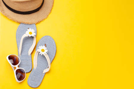 Summer vacation items and accessories. Flip flops, sunglasses and sun hat on yellow background. Top...