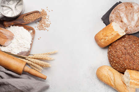 Various bread with wheat, flour and cooking utensils on stone table. Top view flat lay with copy...