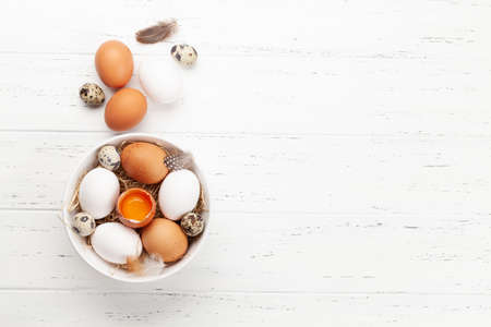 White, brown and quail eggs in bowl on wooden background. Top view with copy space. Flat layの写真素材