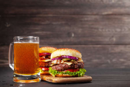 Two homemade tasty burgers with big beef, cheese, tomato, bacon and lettuce and lager beer mug. With copy spaceの写真素材
