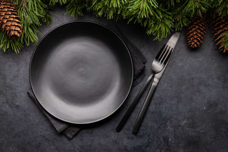 Christmas greeting card with fir tree, empty plate, fork and knife on stone background. Top view flat lay with copy spaceの写真素材