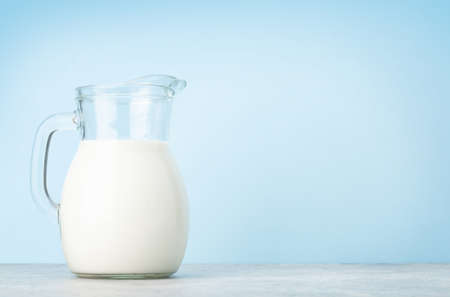 Milk in glass jug in front of blue background with copy spaceの写真素材