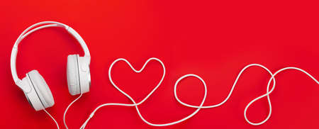 Headphones with heart shaped cable over red backdrop. Love music or Valentines day concept. Top view flat lay with copy spaceの写真素材