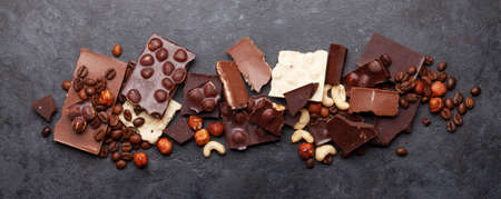Various chocolate pieces, coffee beans and nuts on stone table. Top view flat lay