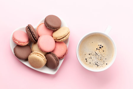 Valentines day with macaroons in heart shaped plate and coffee cup over pink background. Top view flat layの写真素材