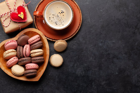 Valentines day with macaroons in heart shaped plate, coffee and gift box over stone background with copy space. Top view flat layの写真素材