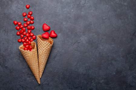 Valentines day greeting card with heart shaped sweets in ice cream waffle cone over stone. Top view flat lay with copy spaceの写真素材
