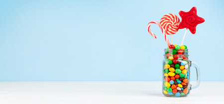 Various sweets assortment. Candy, bonbon, lollipop in glass can over blue background. With copy...