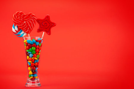Various sweets assortment. Candy, bonbon, chocolate and macaroons in cocktail glass over red background. With copy spaceの写真素材