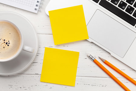 Office desk with yellow stickers, coffee and laptop. Remote office and work from home concept. Top...
