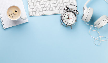 Office desk with supplies, alarm clock and coffee over blue. Creativity and inspiration work concept. Top view flat lay with copy spaceの写真素材