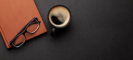 Office desk with supplies and coffee cup over black leather table. Top view flat lay with copy space