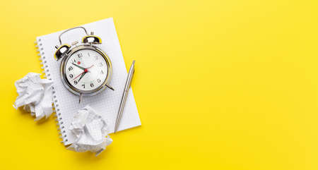 Office desk with alarm clock and blank notepad over yellow. Creativity and inspiration work concept....
