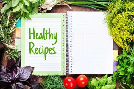 Fresh garden herbs, vegetables and notepad for your healthy recipes on wooden tableの写真素材