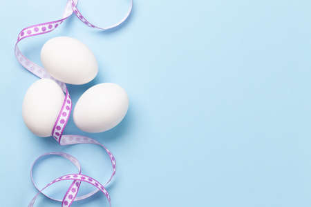 White chicken eggs on blue background. Easter greeting card. Top view with copy space. Flat layの写真素材