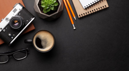 Office desk with supplies, photo camera and coffee over black leather table. Top view flat lay with copy spaceの写真素材