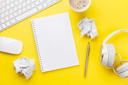 Office desk with supplies, headphones and blank notepad over yellow. Creativity and inspiration work...