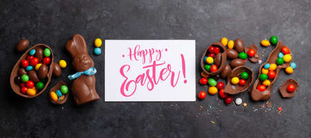 Chocolate easter eggs, choco rabbit and colorful sweets on stone background greeting card. Top view....