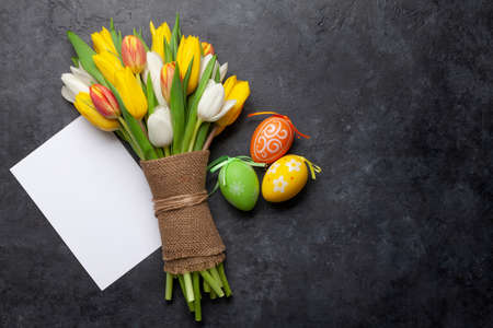 Easter greeting card with easter eggs and tulip flowers over stone background. Top view flat lay with copy spaceの写真素材