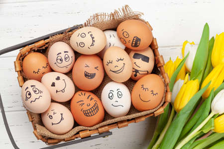 Easter greeting card with easter eggs with funny faces and tulip flowers over stone background. Top view flat layの写真素材