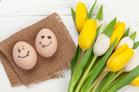 Easter greeting card with easter eggs with funny faces and tulip flowers over wooden background. Top...