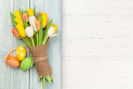Easter greeting card with easter eggs and tulip flowers over wooden background. Top view flat lay...
