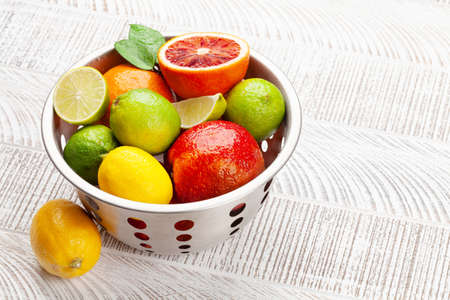 Various fresh citrus fruits in colander. Bood orange, lime, lemon. On wooden table with copy spaceの写真素材